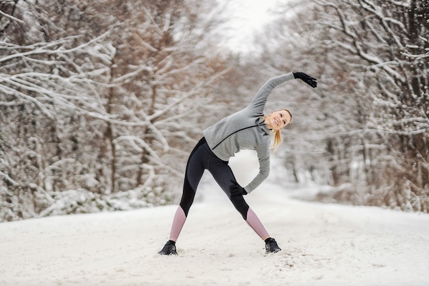 Sportlerin, die am Wintertag in der Natur steht und Aufwärm- und Dehnungsübungen macht. Gesunde Gewohnheiten, Winterfitness, Outdoorfitness