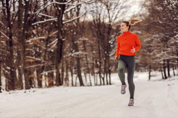 Sportlerin, die an einem verschneiten Wintertag in der Natur joggt. Kaltes Wetter, Schnee, gesundes Leben, Fitness, gesunde Gewohnheiten, Wald