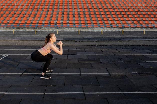 Sportlerin, die Beine für Cardio-Training vorbereitet. Fitness-Läufer, der Aufwärmroutine tut. Frau Läufer im Freien aufwärmen. Sportler, der sich auf einer Laufbahn in einem Stadion ausdehnt und aufwärmt