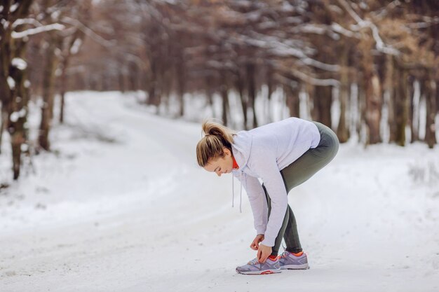 Sportlerin, die im Winter auf Schnee in der Natur steht und Schnürsenkel bindet. Turnschuhe, Winterfitness, gesundes Leben, Natur