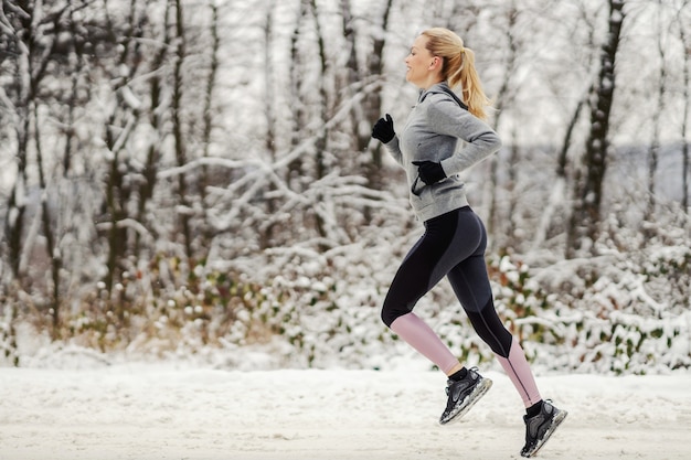 Sportlerin, die im Winter schnell auf schneebedecktem Weg in der Natur läuft.