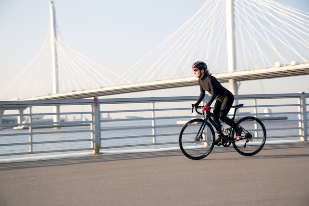 Sportlerin fährt Fahrrad entlang der Böschung vor dem Hintergrund der Brücke