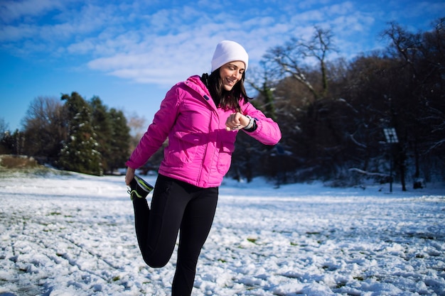 Sportlerin im Winter streckt und wärmt ihren Körper vor dem Training auf Schnee.