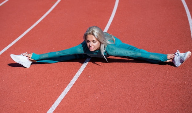 Sportlerin in Sportbekleidung beim Aufwärmen im Stadion vor dem Fitnesstraining, Split-Stretching.