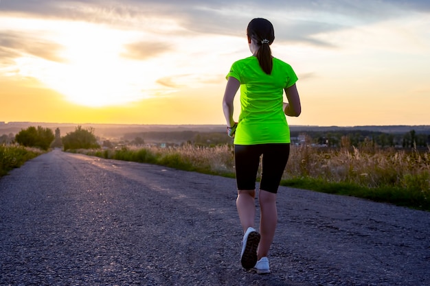 Sportlerin läuft eine Strecke auf der Straße gegen den Sonnenuntergangshimmel