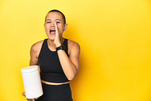 Foto sportlerin mit protein-shake, gelber studio-hintergrund, schreit und hält die handfläche in der nähe des geöffneten mundes