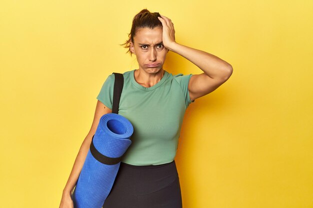 Sportlerin mittleren Alters mit Yogamatte auf gelbem Studio ist schockiert