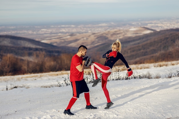 Sportlerin Sparring mit Boxhandschuhen in der Natur am verschneiten Wintertag mit ihrem Trainer.