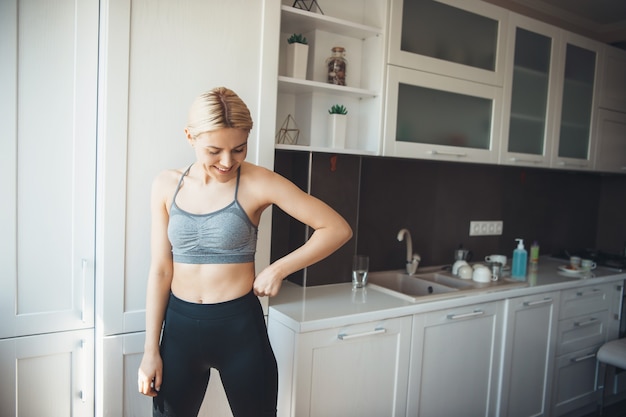 Sportliche blonde Frau, die Sportbekleidung trägt, lächelt in der Küche