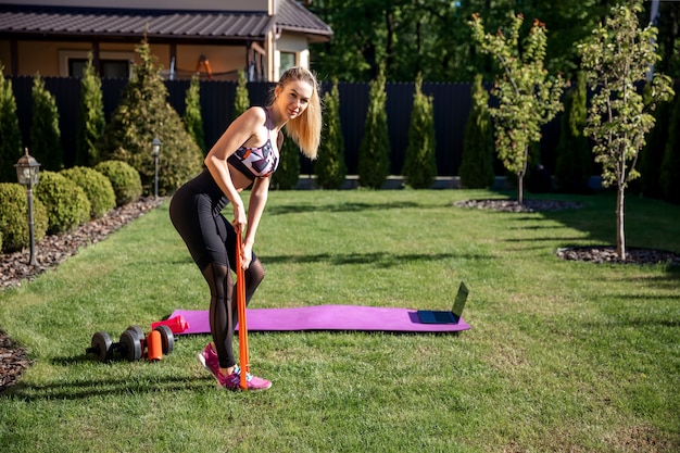 Sportliche Fitnesstrainerin, die Fitnessgummi am Garten mit frischem grünem Gras verwendet