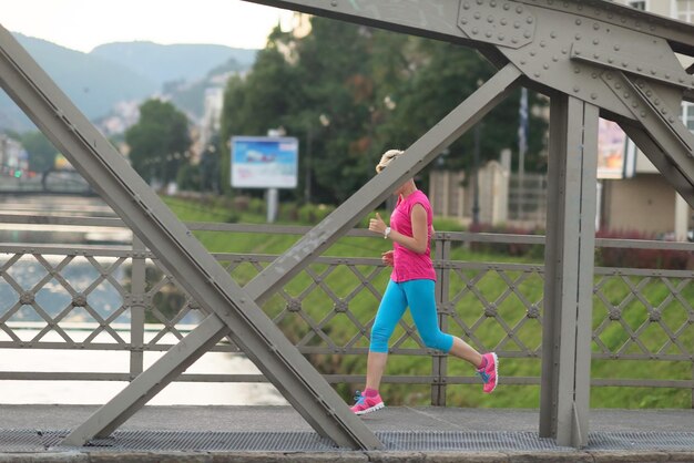 sportliche Frau, die am frühen Morgen auf dem Bürgersteig läuft, mit der Sonnenaufgangsszene der Stadt im Hintergrund