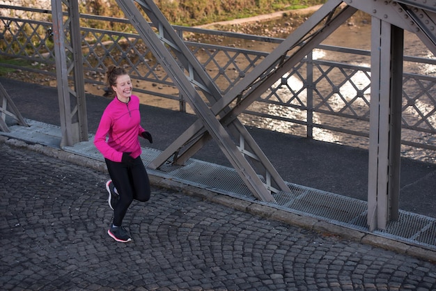 sportliche Frau, die am frühen Morgen auf dem Bürgersteig läuft und mit der Sonnenaufgangsszene der Stadt im Hintergrund joggt