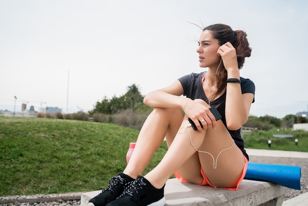 Sportliche Frau, die Musik auf einer Pause vom Training hört.