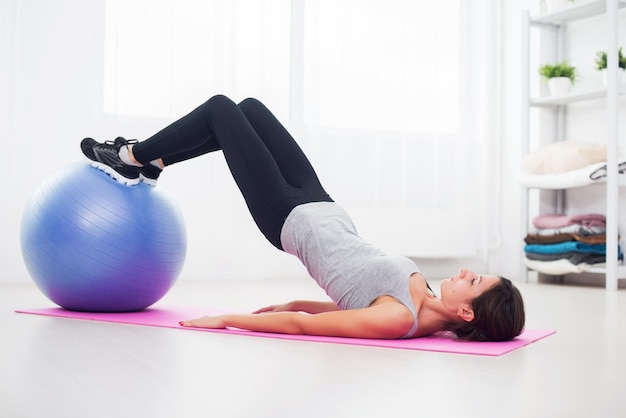 Sportliche Frau, die zu Hause Pilates-Übungen macht, um ihr Becken mit einem fitten Ball anzuheben