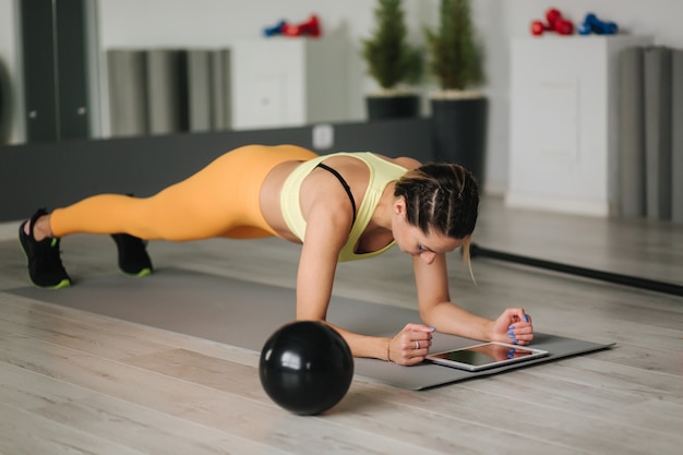 Sportliche Frau in Sportbekleidung macht Übungen zu Hause. Fraublick in Tablette während diong Übungen.