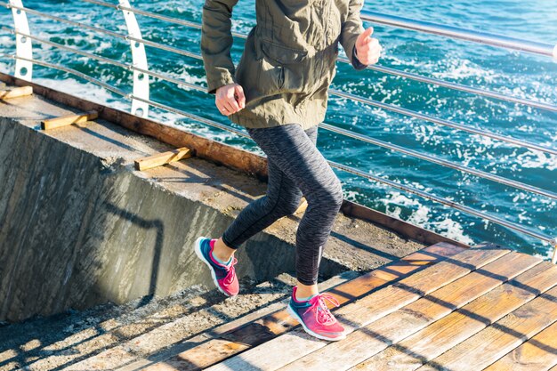 Sportliche Frau in Sportkleidung rennt in Turnschuhen vor dem Hintergrund des Meeres die Treppe hinauf