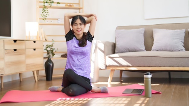 Sportliche Frau sitzt auf einer Matte und streckt Ellbogen und Schulter, nachdem sie zu Hause Yoga gemacht hat