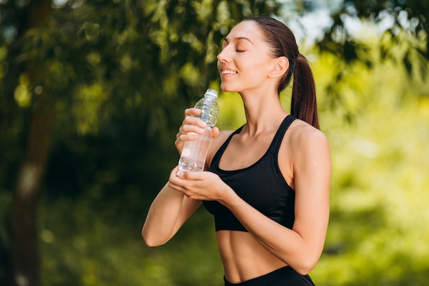 Sportliche Frau trinkt Wasser im Freien mit Vergnügen.
