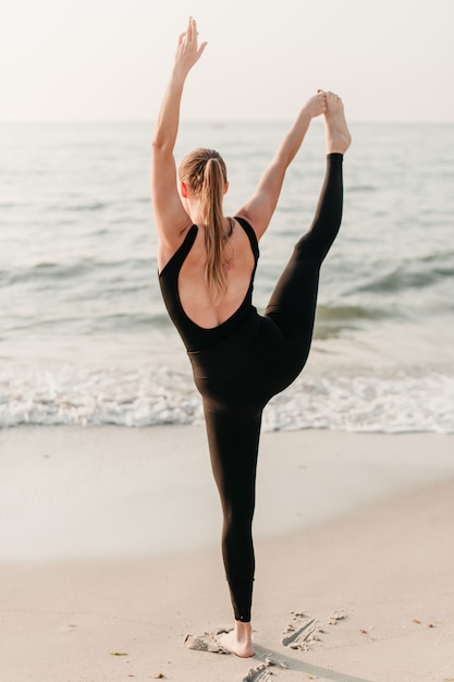 Sportliche junge Frau auf dem Strand üben Yoga asana, das Ozean gegenüberstellt