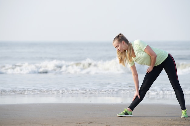 Sportliche junge Frau bücken sich am Strand ausdehnen