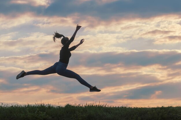 Sportliche junge Frau, die Morgenwolkenhintergrund im Freien springt