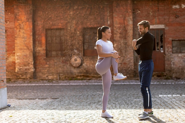 Sportliche junge Frau, die nach dem Joggen mit ihrem persönlichen Trainer Dehnübungen macht