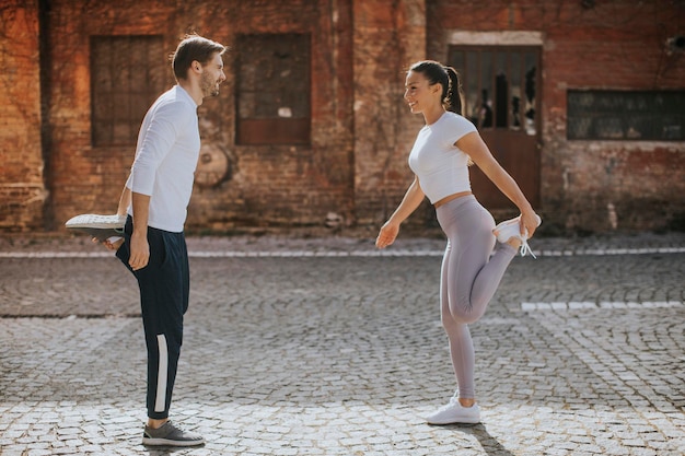 Sportliche junge Frau, die nach dem Joggen mit ihrem persönlichen Trainer Dehnübungen macht