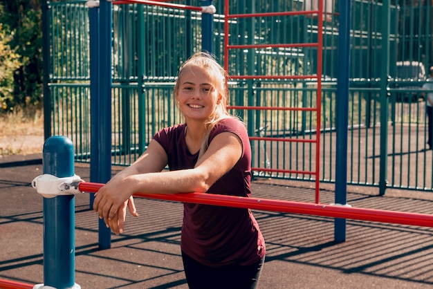 Sportliche junge Frau, die nach dem Training auf dem Sportplatz steht und in die Kamera schaut und lächelt