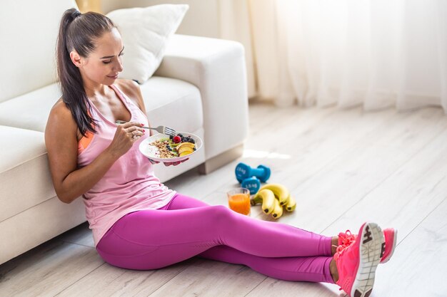 Sportliche junge frau, die nach dem training haferflocken mit beeren und früchten isst