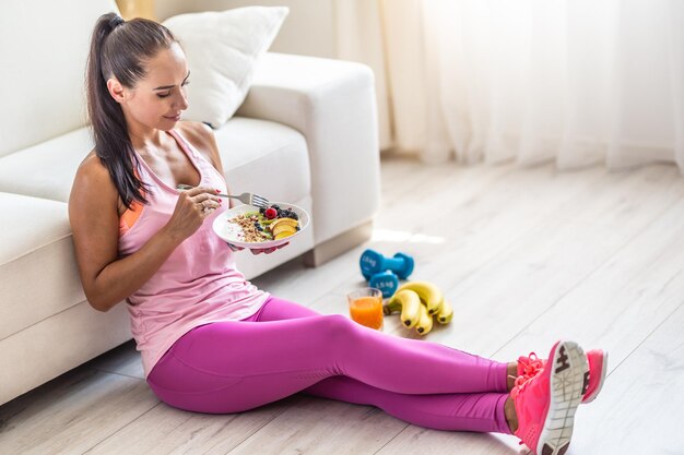 Sportliche junge Frau, die nach dem Training Haferflocken mit Beeren und Früchten isst