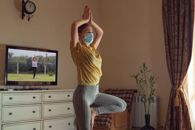 Sportliche junge Frau, die online Yogastunden nimmt und zu Hause übt, während sie in Quarantäne ist.