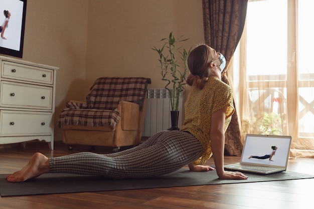 Foto sportliche junge frau, die online yogastunden nimmt und zu hause übt, während sie in quarantäne ist.