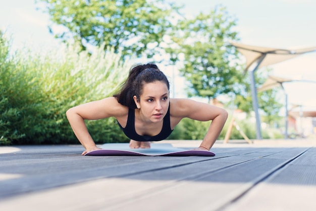 Sportliche junge Frau macht Yoga-Übungen mit Yogamatte im aktiven Lifestyle-Konzept des Parks im Freien