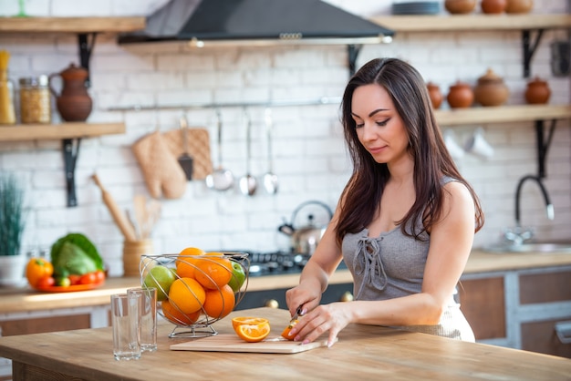 Sportliche junge Frau schneidet frische Orange für Fruchtsaft in der Küche. Horizontale Innenaufnahme.