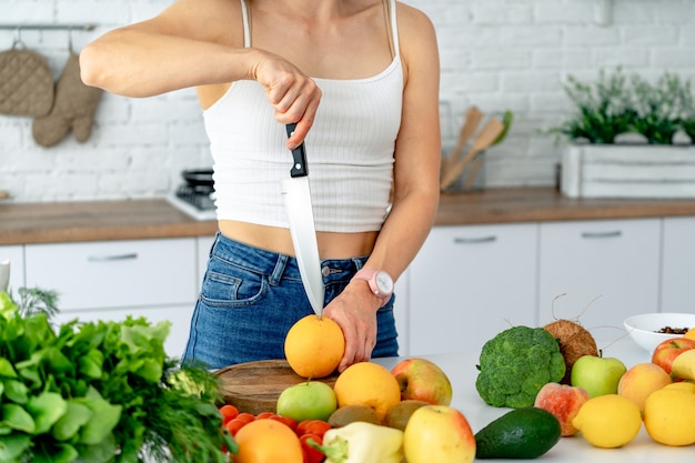 Sportliche junge Frau schneidet frische Orange für Fruchtsaft in der Küche