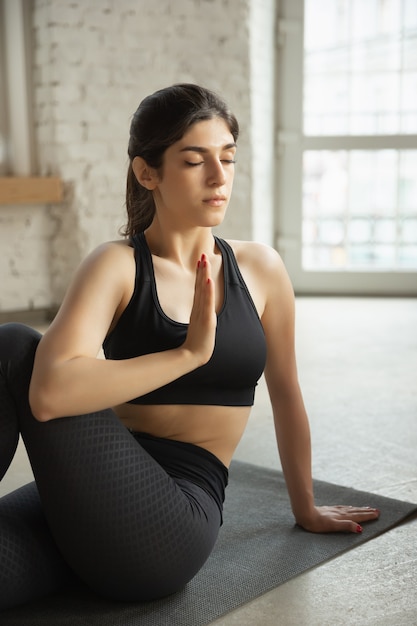 Sportliche junge muslimische Frau, die online Yogastunden nimmt und zu Hause übt