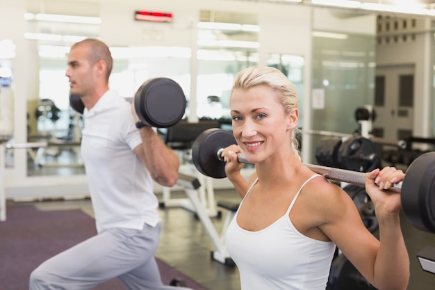 Sportliche junge Paare, die Barbells in der Turnhalle anheben