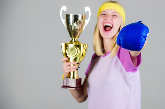 Sportliche Leistung Feiern Sie den Sieg Boxchampion Athletisches Mädchen Boxhandschuh und goldener Kelch Frau trägt Sportoutfit Mädchen fröhlicher Boxer Gewinner Boxen ist mein Hobby Erfolg im Boxen