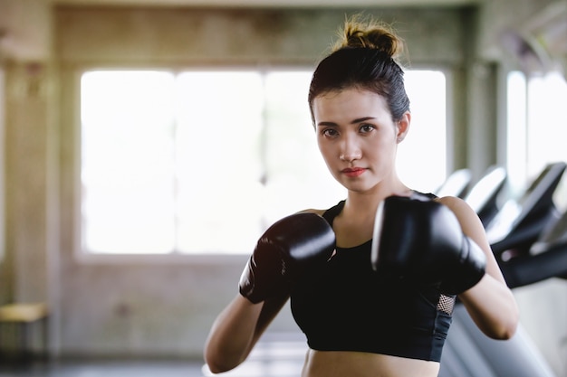 Sportliche mädchenschönheit des porträts mit den hinteren boxhandschuhen ausbildend an der turnhalle