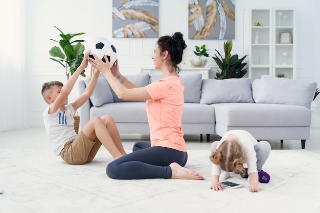 Sportliche Mutter mit Sohn, die morgendliches Training zu Hause macht, während Baby spielt