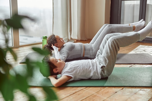 Sportliche Mutter und Sohn beim Bauchmuskeltraining im Haus