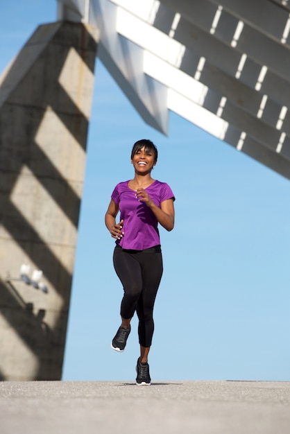 Sportliche schwarze Frau des vollen Körpers, die draußen läuft und lächelt
