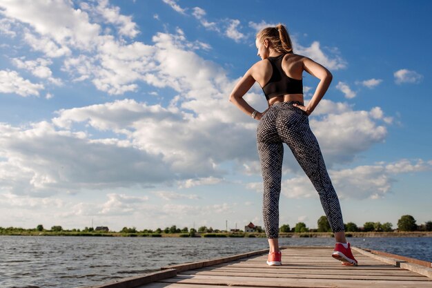 Sportliche sexy Frau in Sportkleidung auf dem Pier auf dem Wasserhintergrund