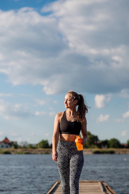 Sportliche sexy Frau in Sportkleidung auf dem Pier auf dem Wasserhintergrund