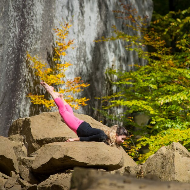 Sportliche Sitzfrau übt Yoga auf dem Flussstein in der Natur