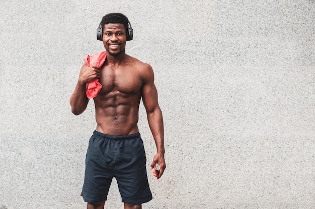 Sportlicher Afroamerikaner steht ohne T-Shirt an der Wand und lächelt