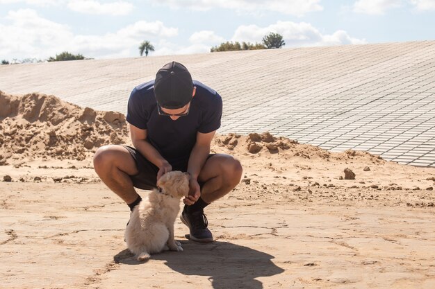 Sportlicher Junge, der seinen Welpen im Sand streichelt.