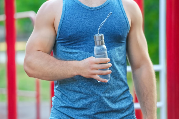 Sportlicher junger Mann mit einer Flasche Wasser im Freien