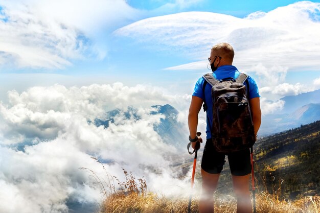 Sportlicher kerl reisender mit rucksack auf dem hintergrund eines schönen himmels mit wolken in den bergen über den wolken indonesien rinjani gunung