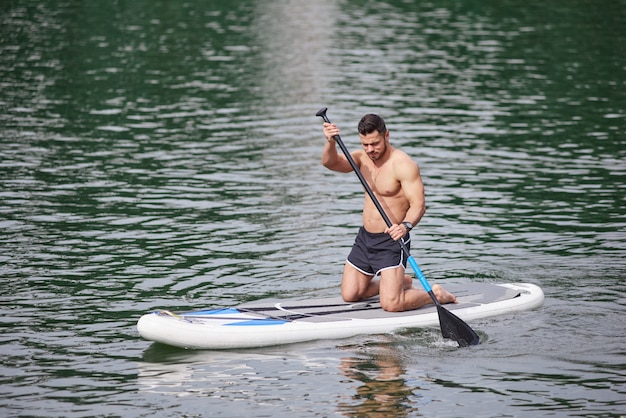 Sportlicher Mann, der das Ruder hält und seine supboarding Fähigkeiten ausbildet.